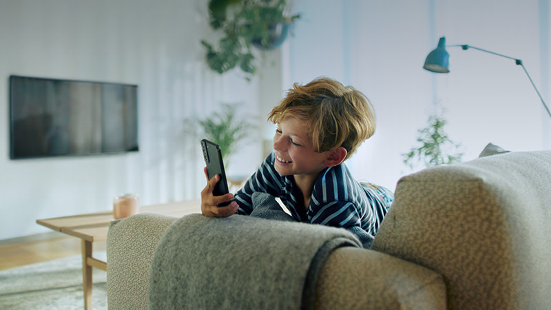 Pojke som sitter i soffa med mobil i handen