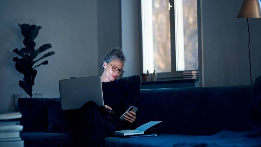 Kvinna i soffan med mobil och dator i handen