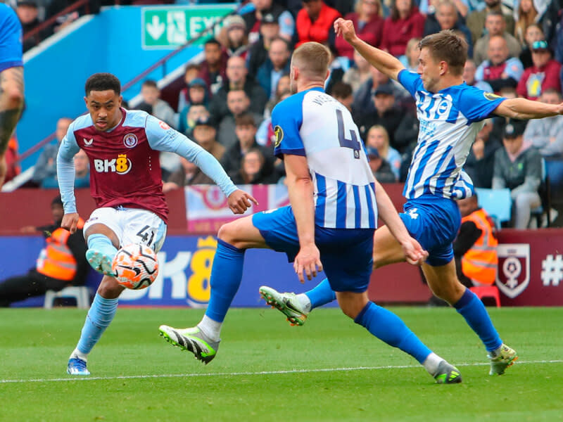 En spelare i Aston Villa skjuter bollen, medan försvarare i Brighton försöker stoppa skottet.